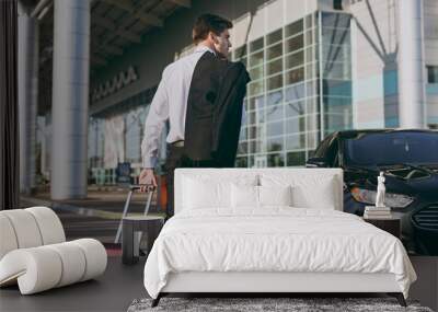 Bottom back rear view young traveler businessman young man wearing black dinner suit walk go outside at international airport terminal with suitcase to car book taxi Air flight business trip concept Wall mural