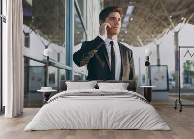 Bottom view young traveler businessman man in black suit stand outside at international airport terminal talk on mobile cell phone book taxi order hotel look aside Air flight business trip concept Wall mural