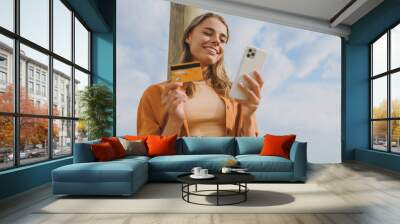 Bottom view young woman wears orange shirt casual clothes using mobile cell phone credit bank card shopping online walk on sea ocean sand shore beach outdoor seaside in summer day. Lifestyle concept. Wall mural