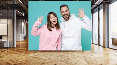 Cheerful excited young couple two friends man woman 20s wearing white pink casual hoodie standing showing OK gesture looking camera isolated on blue turquoise colour wall background studio portrait. Wall mural