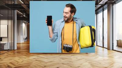 Cheerful traveler tourist man in summer clothes with photo camera isolated on blue background. Passenger traveling abroad on weekends. Air flight journey. Hold suitcase mobile phone with blank screen. Wall mural