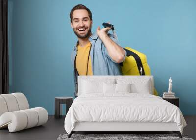 Cheerful traveler tourist man in yellow summer casual clothes with photo camera isolated on blue background. Male passenger traveling abroad on weekends. Air flight journey concept. Holding suitcase. Wall mural