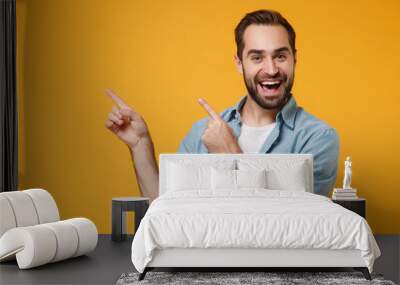 Cheerful young bearded man in casual blue shirt posing isolated on yellow orange background studio portrait. People sincere emotions lifestyle concept. Mock up copy space. Pointing index fingers up. Wall mural