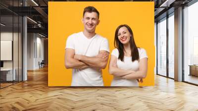 Cheerful young couple two friends guy girl in white empty blank design t-shirts posing isolated on yellow orange wall background. People lifestyle concept. Mock up copy space. Holding hands crossed. Wall mural