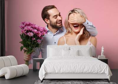 Cheerful young couple two guy girl in party outfit celebrating isolated on pastel pink background. Valentine's Day Women's Day birthday holiday concept. Hold bouquet of flowers, cover eyes with hand. Wall mural