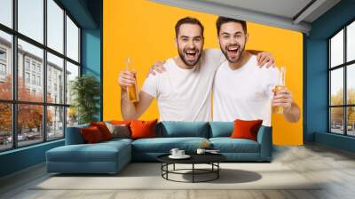 Cheerful young men guys friends in white empty blank t-shirts posing isolated on yellow orange wall background. People emotions lifestyle concept. Mock up copy space. Hugging, holding beer bottles. Wall mural