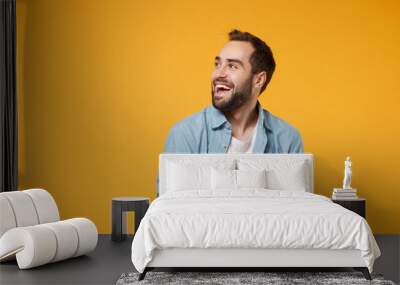 Cheerful young student man in casual blue shirt posing isolated on yellow orange wall background, studio portrait. People lifestyle concept. Mock up copy space. Writing note in notebook looking aside. Wall mural