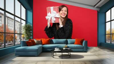 Cheerful young woman in fur sweater hold red striped present box with gift ribbon isolated on red background. Valentine's Day, International Women's Day, birthday, holiday concept. Mock up copy space. Wall mural