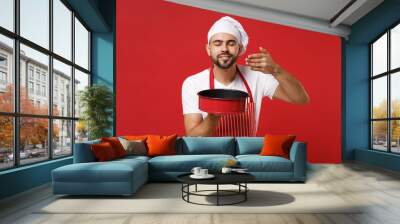 Chef cook or baker man in striped apron toque chefs hat posing isolated on red background. Cooking food concept. Mock up copy space. Hold baking form for pie, raised hand to face, feeling food smell. Wall mural