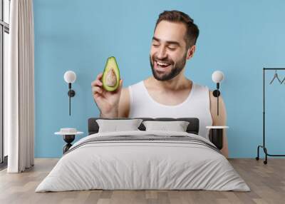 Close up bearded young man 20s years old in white shirt hold half of avocado isolated on blue pastel background, studio portrait. Skin care healthcare cosmetic procedures concept. Mock up copy space. Wall mural