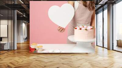 Close up cropped chef cook confectioner or baker in apron white t-shirt cooking cake or cupcake at table hold like heart isolated on pink pastel background in studio. Mock up copy space food concept. Wall mural