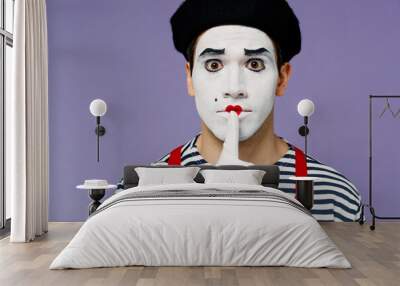 Close up secret vivid young mime man with white face mask wears striped shirt beret say hush be quiet with finger on lips shhh gesture isolated on plain pastel light violet background studio portrait. Wall mural