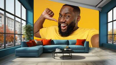 Close up young fun happy black man 20s in bright casual t-shirt doing selfie shot pov on mobile phone point finger on himself isolated on plain yellow color background stuio. People lifestyle concept. Wall mural