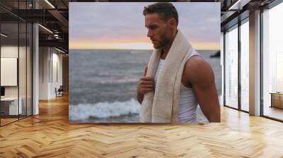 Close up young strong sporty athletic toned fit sportsman man he wear sports clothes white towel walk go warm up training at sunrise sun dawn over sea beach outdoor on seaside in summer day morning. Wall mural