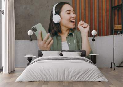 Close up young woman wear casual clothes headphones listen music use mobile cell phone microphone sing sit on grey sofa couch stay at home hotel flat rest relax spend free spare time in living room. Wall mural