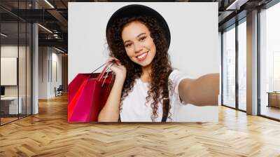 Close up young woman wear t-shirt hat hold in hand red paper package bag after shopping do selfie shot pov mobile cell phone isolated on plain solid white background Black Friday sale buy day concept Wall mural