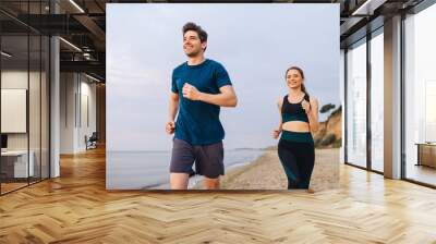 Couple young two friend strong sporty athletic sportswoman sportsman woman man in sport clothes warm up training running on sand sea ocean beach outside jog on seaside in summer day cloudy morning. Wall mural