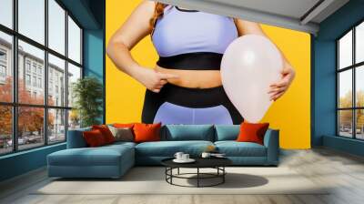 Cropped young chubby overweight plus size big fat fit woman wears blue top warm up training hold in hand ballon near stomach isolated on plain yellow background studio home gym. Workout sport concept. Wall mural