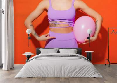 Cropped young fitness trainer instructor sporty woman sportsman in purple top clothes in home gym hold pink balloon near belly isolated on plain orange background Workout sport fit abs diet concept Wall mural