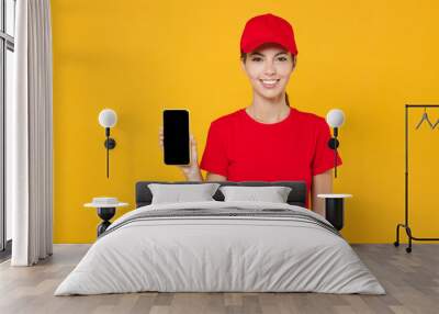 Delivery employee woman in red cap blank t-shirt uniform work courier in service during quarantine coronavirus covid-19 virus hold mobile phone black screen mockup isolated on yellow background studio Wall mural