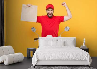 Delivery man in red cap t-shirt uniform driving moped motorbike scooter hold craft paper packet with food isolated on yellow background studio Guy employee working courier Service quarantine concept Wall mural