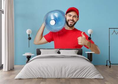 Delivery man in red uniform cap t-shirt print workwear carrying bottle of water to office cooler isolated on blue background studio portrait. Male employee courier. Service concept. Mock up copy space Wall mural