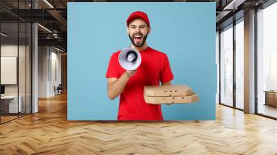 Delivery man in red workwear giving food order pizza boxes isolated on blue background, studio portrait. Professional male employee in cap t-shirt print courier. Service concept. Mock up copy space. Wall mural