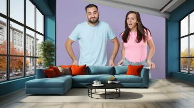 Displeased confused young couple two friends man woman in blue pink blank design t-shirts having no money showing empty pockets looking camera isolated on pastel violet background studio portrait. Wall mural