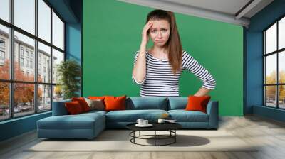 Displeased dissatisfied upset crying young brunette woman 20s wearing striped casual clothes posing put hand on head having headache looking camera isolated on green color background, studio portrait. Wall mural