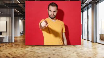 displeased young bearded man guy in casual yellow t-shirt posing isolated on red background studio p Wall mural