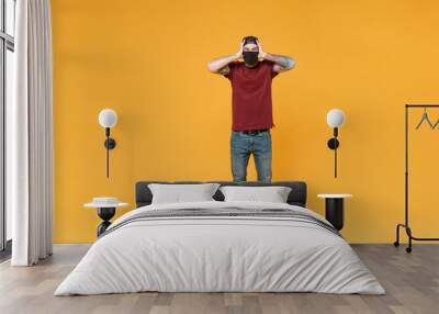 Displeased young tattooed man guy in casual t-shirt cap black face mask posing isolated on yellow background studio portrait. People emotions lifestyle concept. Mock up copy space. Put hands on head. Wall mural