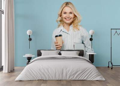 Elderly smiling happy woman 50s wear striped shirt hold use work on laptop pc computer hold takeaway delivery craft paper brown cup coffee to go isolated on plain pastel light blue color background Wall mural