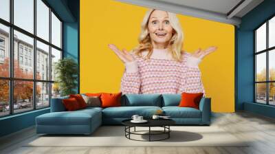 Elderly surprised shocked amazed excited blonde caucasian woman 50s in pink sweater spread hand say wow awesome cool isolated on plain yellow color background studio portrait People lifestyle concept Wall mural