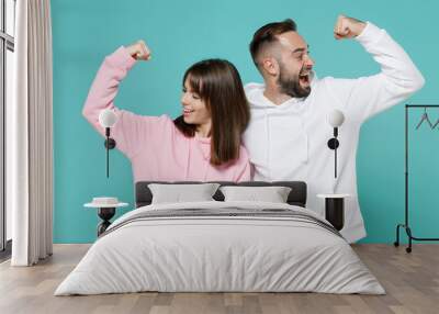 Excited cheerful young couple two friends man woman 20s wearing white pink casual hoodie standing showing biceps muscles looking aside isolated on blue turquoise colour background studio portrait. Wall mural