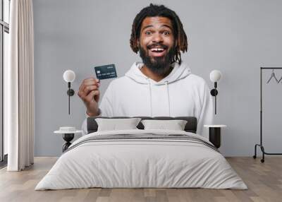 Excited young african american man guy with dreadlocks 20s wearing white casual streetwear hoodie posing hold credit bank card keeping mouth open isolated on grey color background studio portrait. Wall mural