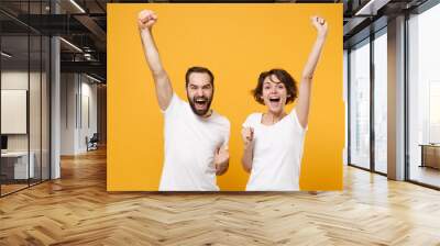 Excited young couple friends bearded guy girl in white empty blank t-shirts posing isolated on yellow orange background. People lifestyle concept. Mock up copy space. Doing winner gesture, screaming. Wall mural