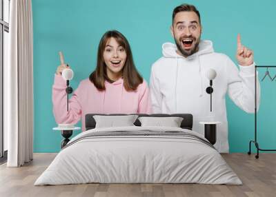 Excited young couple two friends man woman 20s wearing white pink casual hoodie standing holding index finger up with great new idea isolated on blue turquoise colour wall background studio portrait. Wall mural