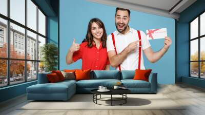 Excited young couple two friends man woman wearing white red clothes pointing index finger on gift certificate showing thumb up isolated on blue background studio. St. Valentine's Day holiday concept. Wall mural