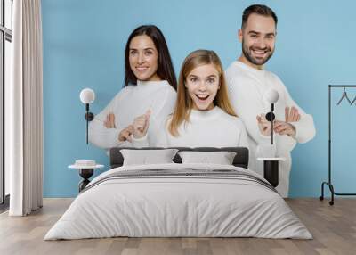 Excited young parents mom dad with child kid daughter teen girl in white sweaters hold hands crossed doing winner gesture isolated on blue background studio. Family day parenthood childhood concept. Wall mural