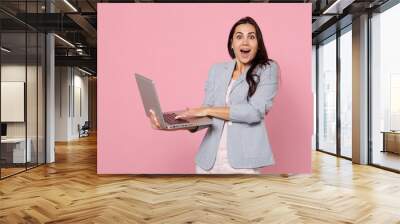 Excited young woman in striped jacket using laptop pc computer keeping mouth wide open isolated on pink pastel wall background in studio. People sincere emotions lifestyle concept. Mock up copy space. Wall mural