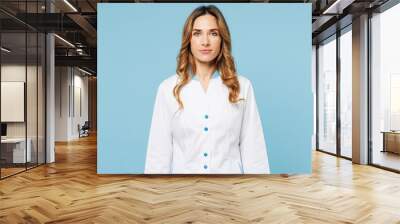 Female serious confident Caucasian doctor woman she wears white medical gown suit work in hospital clinic office looking camera isolated on plain blue background studio. Health care medicine concept. Wall mural