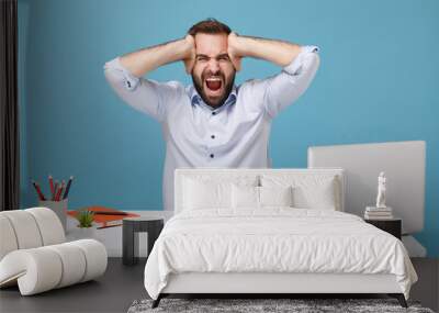 Frustrated man in shirt sit work at desk with pc laptop isolated on blue background. Achievement business career lifestyle concept. Mock up copy space. Screaming keeping eyes closed put hands on head. Wall mural