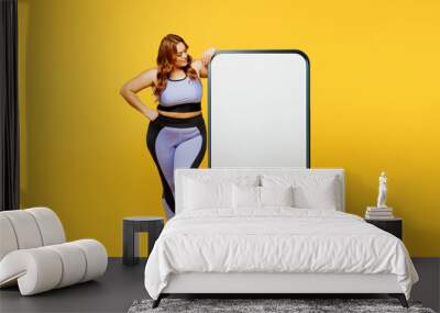 Full body fun young plus size big fat fit woman wear blue top warm up train look at big huge blank screen mobile cell phone isolated on plain yellow background studio home gym. Workout sport concept. Wall mural