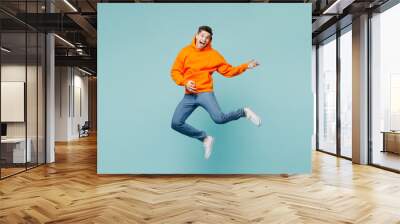 Full body happy singer young man he wears orange hoody casual clothes jump high play do air guitar gesture isolated on plain pastel light blue cyan color background studio portrait. Lifestyle concept. Wall mural