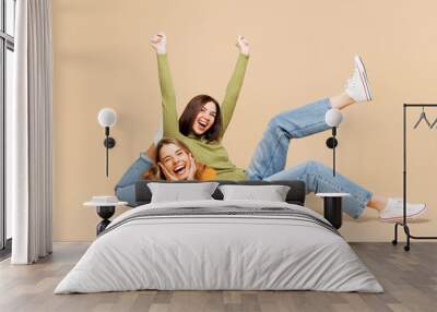 Full body happy young friends two women wear orange green shirt casual clothes together sit lay down raise up leg hands do winner gesture isolated on plain pastel beige background. Lifestyle concept. Wall mural