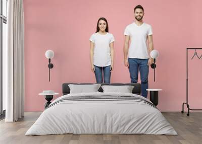 Full body length young cheerful couple two friends bearded man brunette woman in white basic blank print design t-shirts jeans standing posing isolated on pastel pink color background studio portrait. Wall mural