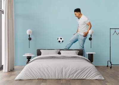 Full body side profile view happy cheerful young man fan wear t-shirt cheer up support football sport team hit soccer ball on leg watch tv live stream isolated on plain pastel blue color background. Wall mural