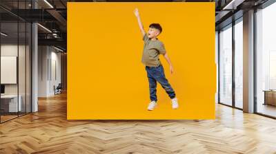 Full body side view little small smiling happy boy 6-7 years old wear green t-shirt walk go waving hand isolated on plain yellow background studio portrait. Mother's Day love family lifestyle concept. Wall mural