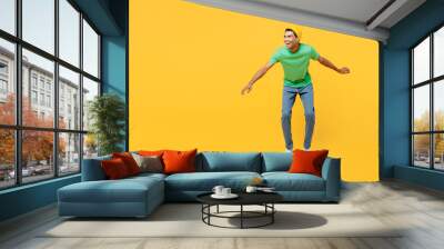 Full body side view smiling young man of African American ethnicity he wears casual clothes green t-shirt hat rising skateboard isolated on plain yellow background studio portrait. Lifestyle concept. Wall mural