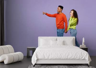 Full body side view young couple two friend family man woman of African American ethnicity in casual clothes hold hands walk go together point finger aside isolated on pastel plain purple background Wall mural